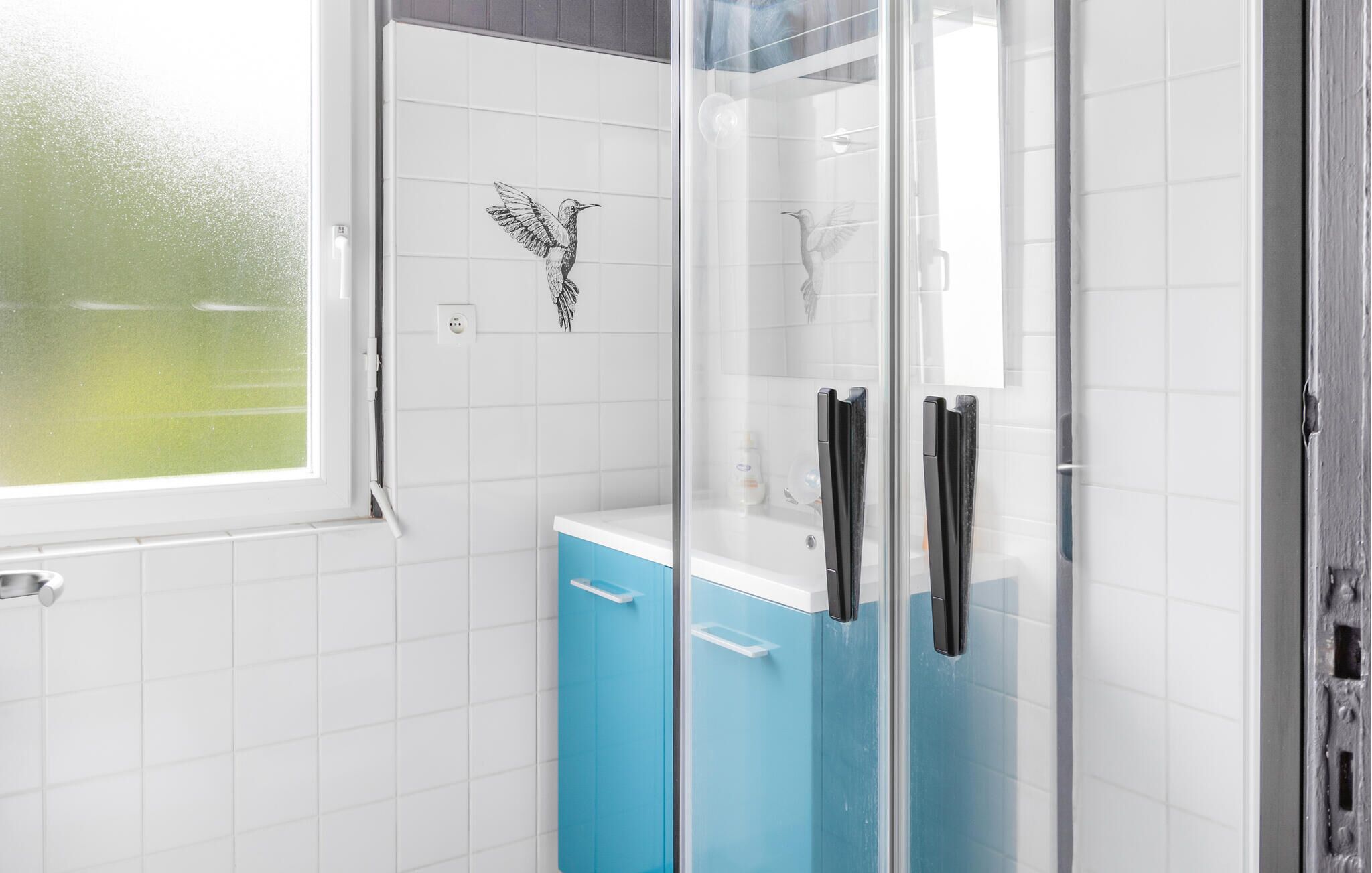 Une salle de bain moderne avec une douche à l’italienne en verre, des murs recouverts de carreaux blancs et une fenêtre.