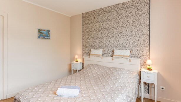 Een slaapkamer met een bed, twee nachtkastjes, een wand met een bladpatroon en een klein schilderij.