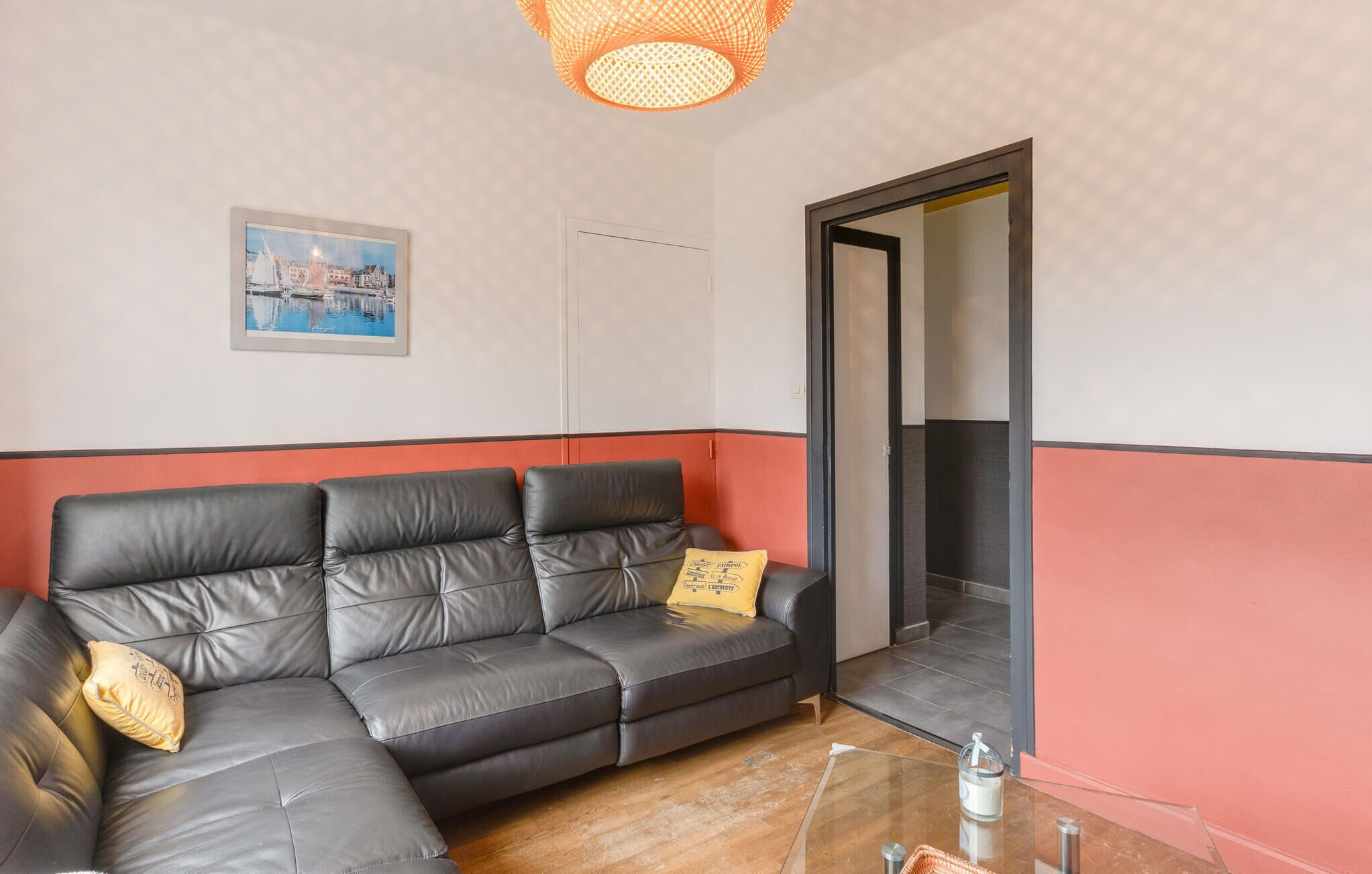 A living room with a sectional sofa, a glass coffee table, a framed picture on the wall, and a door leading to another room.