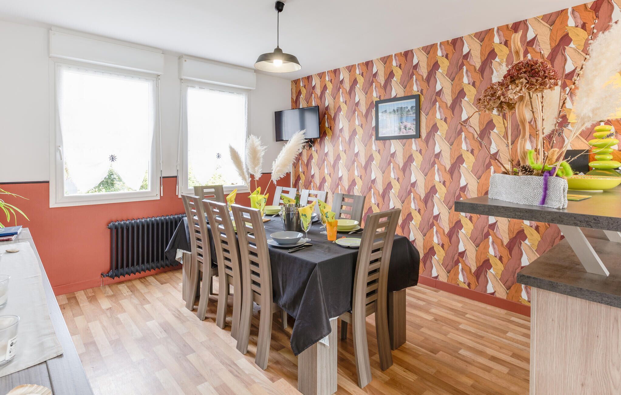 Un coin repas avec une table dressée pour quatre personnes, un radiateur et un mur orné d’un motif de feuilles.