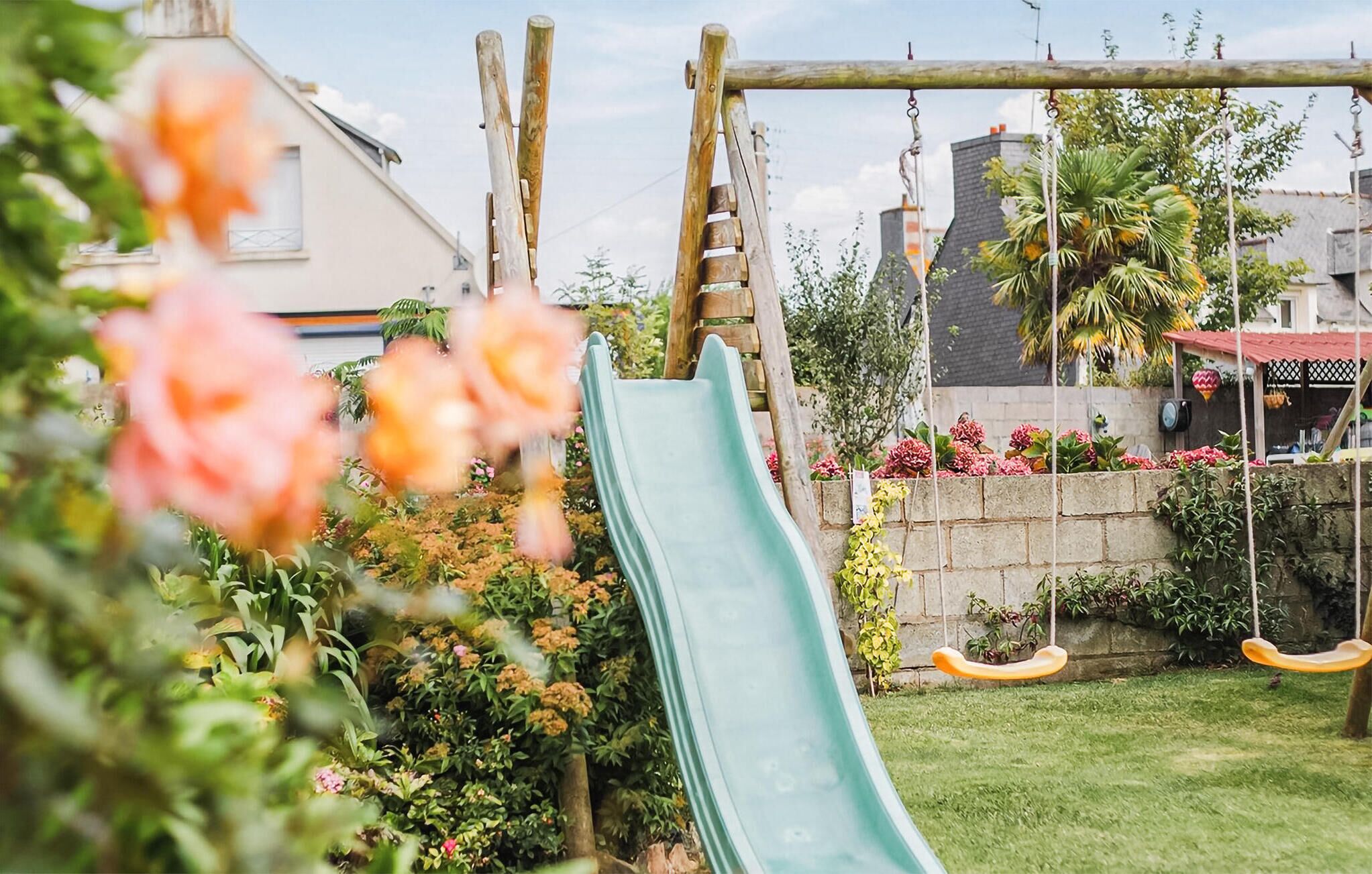 A backyard with a slide, a swing set, and a garden with flowers and plants.