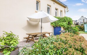 A patio with a wooden table and a white umbrella, surrounded by greenery and a building. - Awesome home in Lézardrieux with WiFi (Lézardrieux)