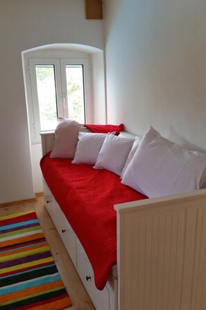 Ein Schlafzimmer mit einem Bett, einem Fenster, einem farbenfrohen Streifen Teppich und einer weißen Heizung.