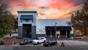 A restaurant with a modern design, a parking lot with several cars, and a sunset sky.