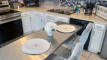 A modern kitchen with white cabinets, a stainless steel countertop, a built-in oven, a microwave, and a coffee station.