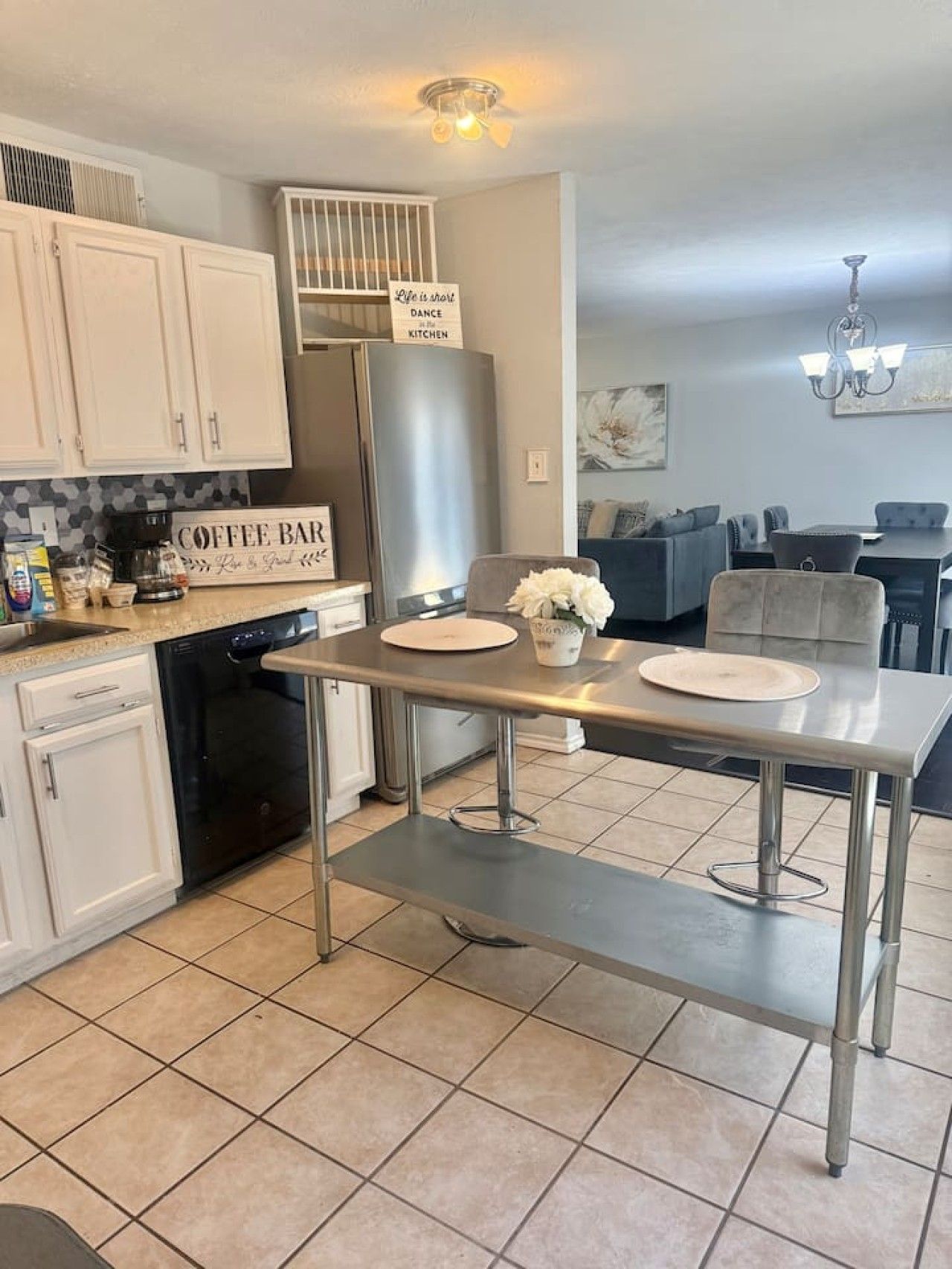 A modern kitchen with a dining area, featuring a stainless steel refrigerator, a coffee bar sign, and a dining table with chairs.