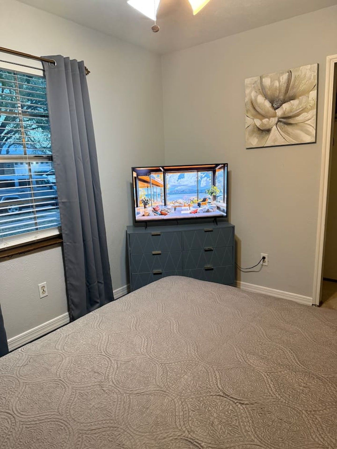 A bedroom with a bed, a dresser, a TV, and a window with curtains.