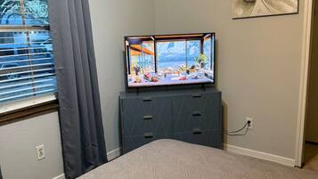 A bedroom with a bed, a dresser, a TV, and a window with curtains.