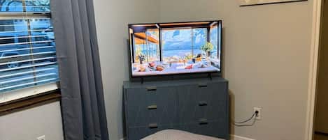 Ein Schlafzimmer mit einem Bett, einem Schminktisch, einem Fernseher und einem Fenster mit Vorhängen.