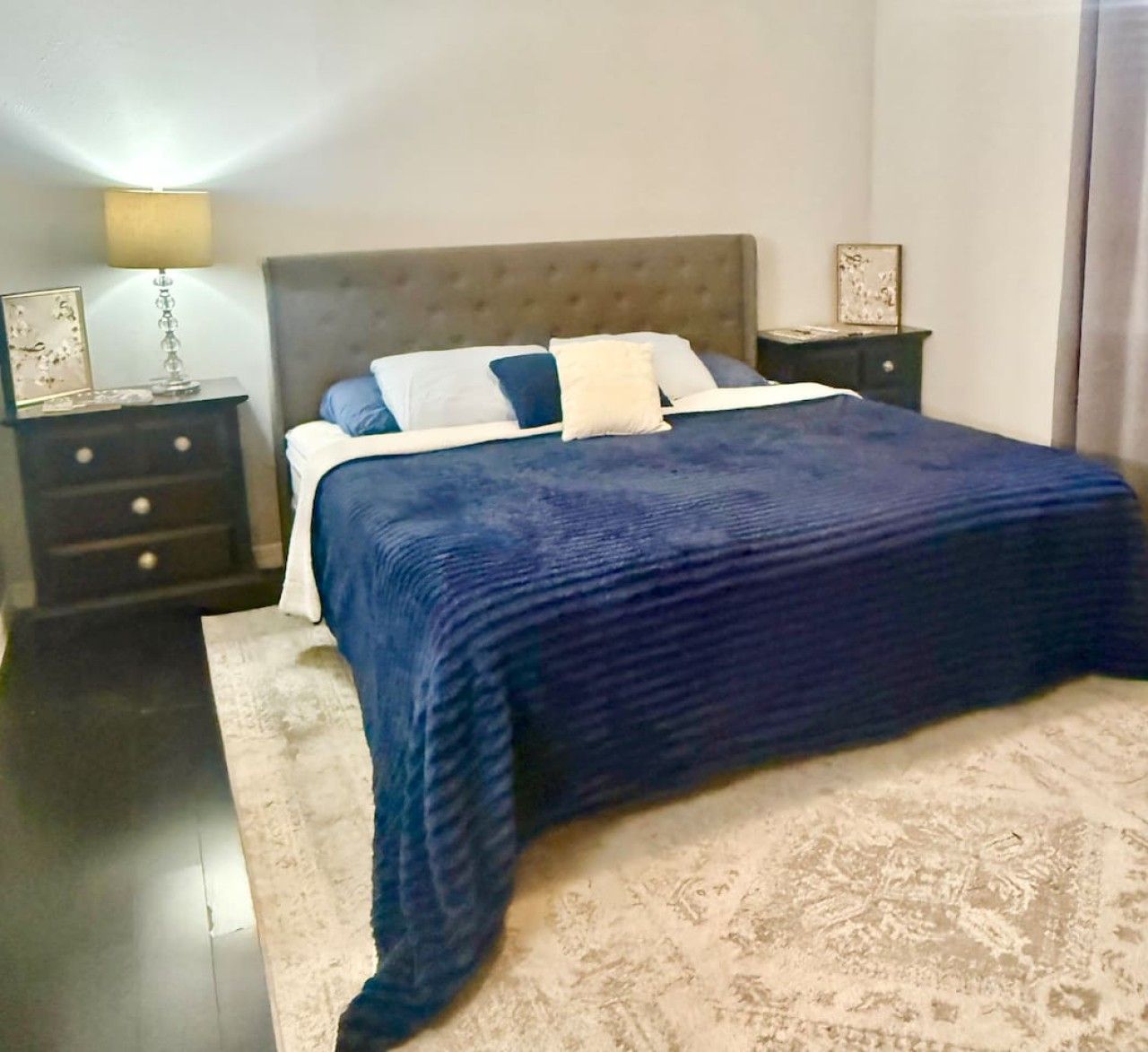Un dormitorio con cama, mesitas de noche, lámpara y alfombra.