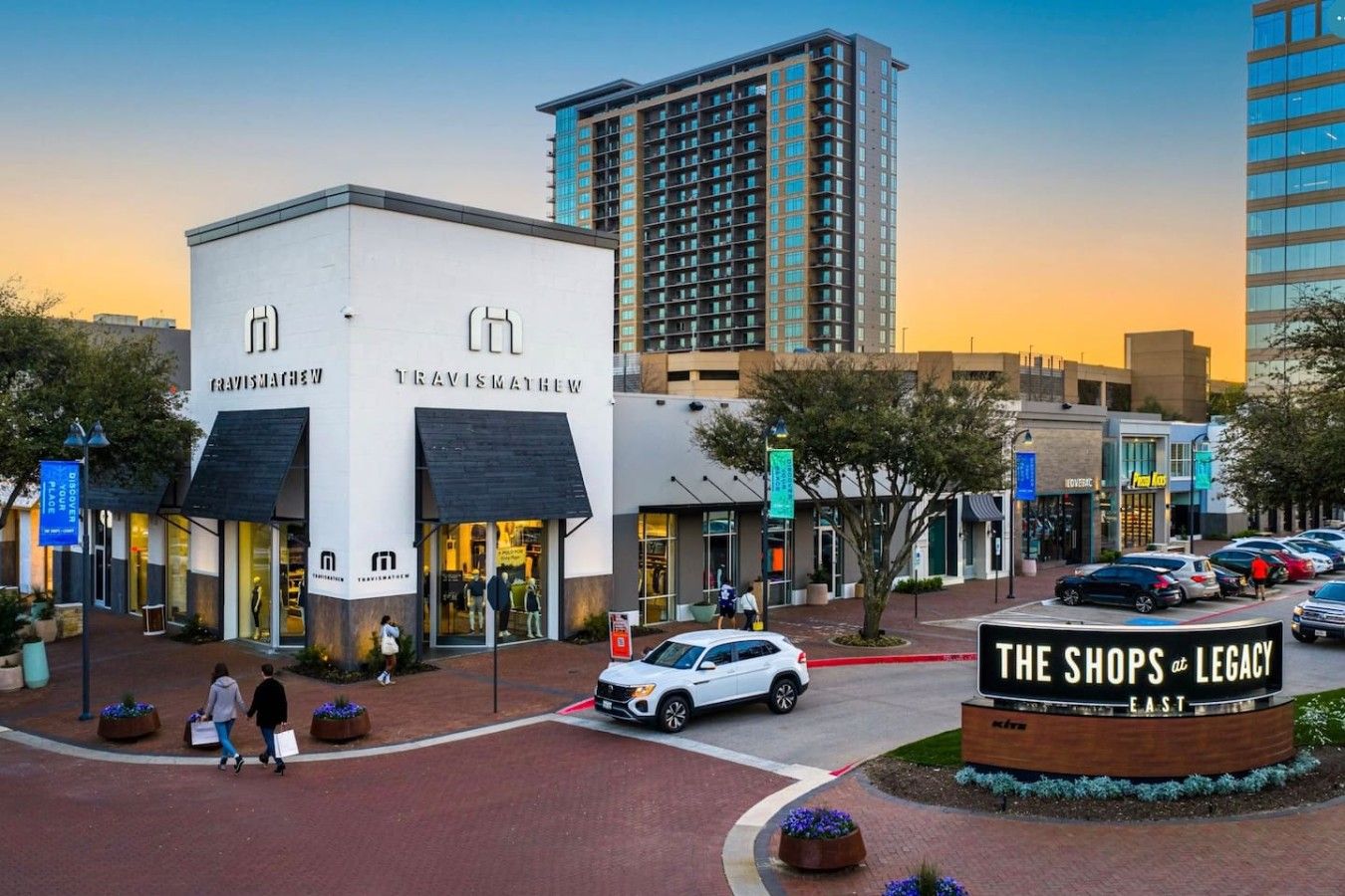 Une zone commerciale avec un bâtiment blanc portant l’inscription « TRAVISMATHEW » et un panneau indiquant « THE SHOPS at LEGACY EAST ».