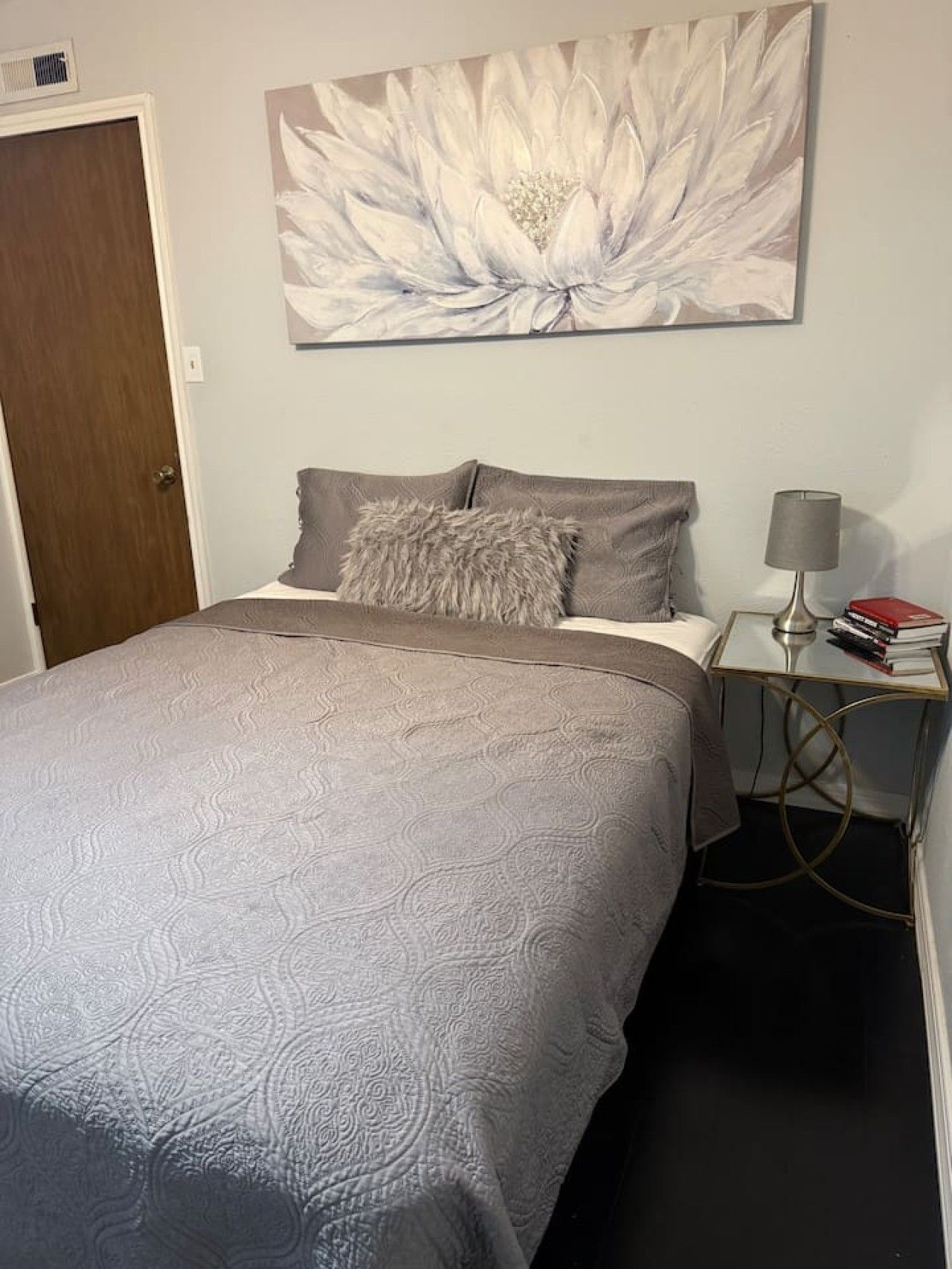 A bedroom with a bed, a nightstand with a lamp, and a wall-mounted artwork.