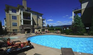 A swimming pool area with lounge chairs and a building with multiple balconies. - Spacious 3BR Condo with Pool, Hot Tub & Golf Views - 2110 (Kelowna)