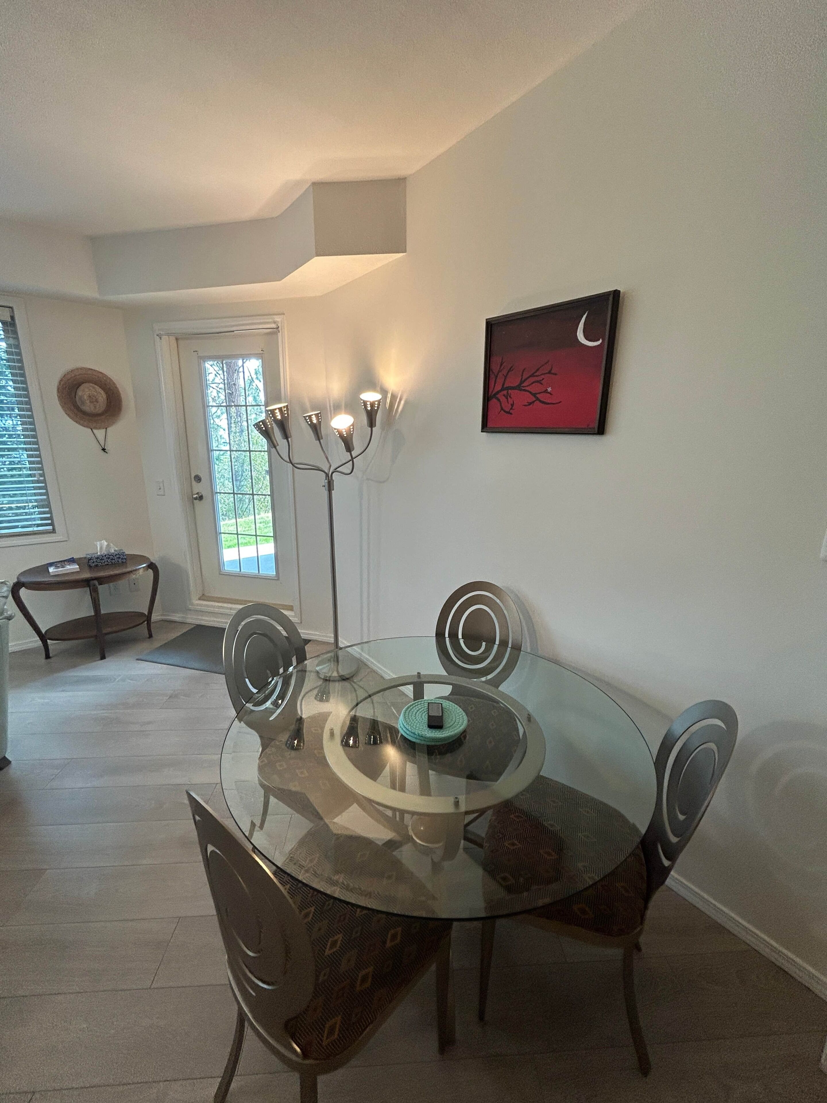 A dining area with a glass table, chairs, and a floor lamp.