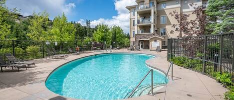 A swimming pool with a 3 ft 4 in depth marker, surrounded by lounge chairs and a multi-story building with balconies.