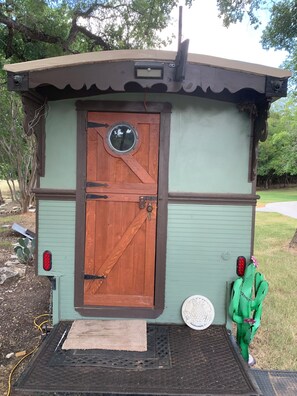 A small, rustic cabin with a wooden door, a circular window, and a metal roof.