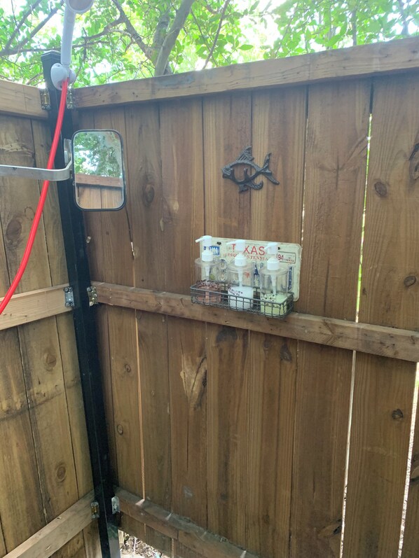 A wooden fence with a metal shelf holding several bottles, a small mirror, and a decorative metal piece.