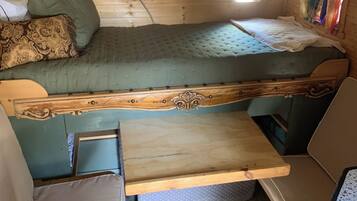 A compact RV interior with a bunk bed, a small kitchenette, and a window providing natural light.