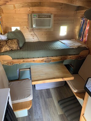 A compact RV interior with a bunk bed, a small kitchenette, and a window providing natural light.