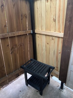 A black metal bench in a corner with a wooden fence in the background.