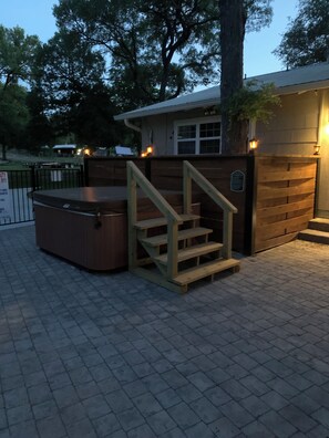 A hot tub with a wooden staircase leading to a covered area, surrounded by a brick patio and a wooden fence. -     Gypsy Mini Charming Tiny Cabin at Red Canoe Lodge with Resort Amenities (Clifton)