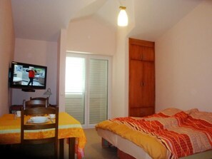 Een slaapkamer met een bed, een bureau met stoel, een televisie en een kledingkast.