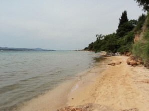 Ein Strand mit klarem Wasser, sandigem Ufer und einer bewaldeten Klippe.