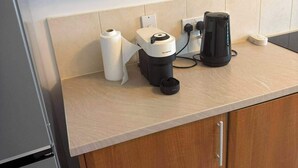 A kitchen with a coffee machine, a roll of paper towels, and a kettle on the counter. - Apartment Sleeps 6 with Parking (Stanmore)