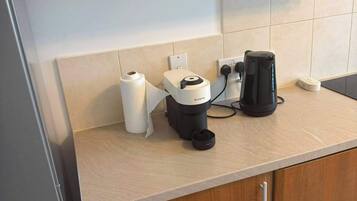 Cuina amb una cafetera, un rotllo de paper de cuina i un bllotge al taulell.