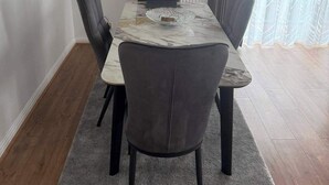 A dining area with a marble table, grey upholstered chairs, a grey rug, and a window with grey curtains. - Apartment Sleeps 6 with Parking (Stanmore)