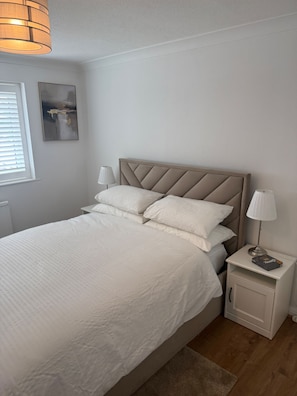 A neatly made bed with a headboard, a bedside lamp, and a small bedside table with a book.