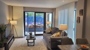 A modern living room with a sofa, a coffee table, a TV, and a dining area with a bowl of fruit. - Cozy Central London, Zone 1 Apartment, sleeps 5 (London)