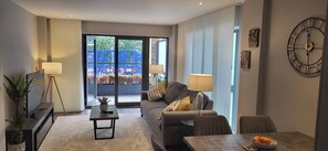 Ein modernes Wohnzimmer mit Sofa, Couchtisch, Fernseher und einem Essbereich mit einer Obstschale.