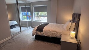 A bedroom with a bed, bedside table, and a lamp. There are large windows and a view of the outside. - Cozy Central London, Zone 1 Apartment, sleeps 5 (London)