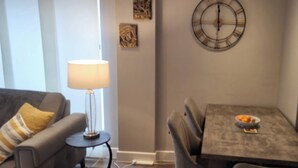 A living room with a sofa, a table with chairs, a lamp, and a wall clock. - Cozy Central London, Zone 1 Apartment, sleeps 5 (London)