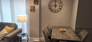 Ein Wohnzimmer mit einer Couch, einem Tisch mit Stühlen, einer Lampe und einer Wanduhr.