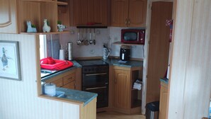 A compact kitchen with wooden cabinets, a stove, a microwave, and various kitchen utensils.