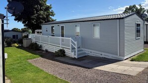 A single-story mobile home with a white exterior, a small porch with a white railing, and a gravel driveway. - 2 x Cabin Retreat in Coldingham (Coldingham)