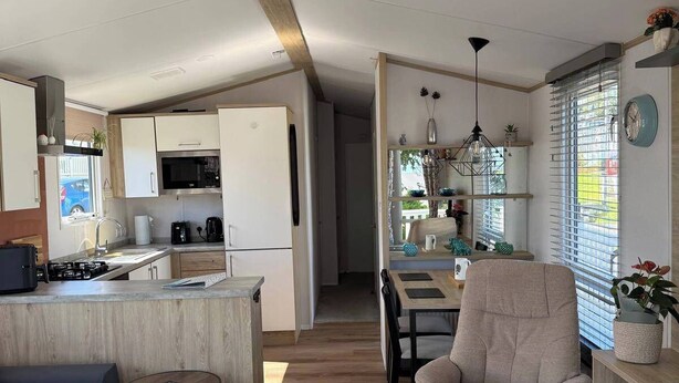 A modern kitchen with white cabinets, a microwave, and a coffee machine. There is a dining area with a table and chairs, and a sofa in the living room. - 2 x Cabin Retreat in Coldingham (Coldingham)
