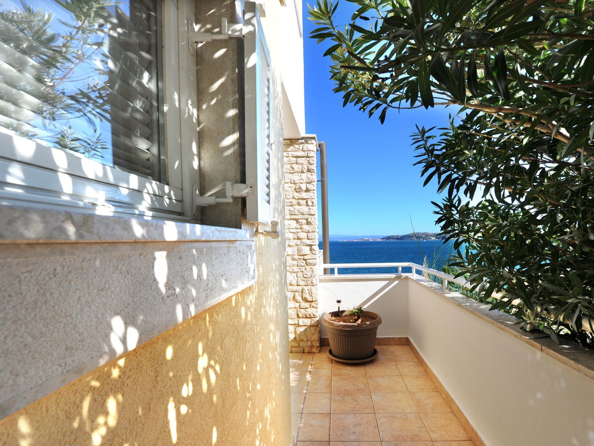 A balcony with a stone pillar, a potted plant, and a view of the sea.