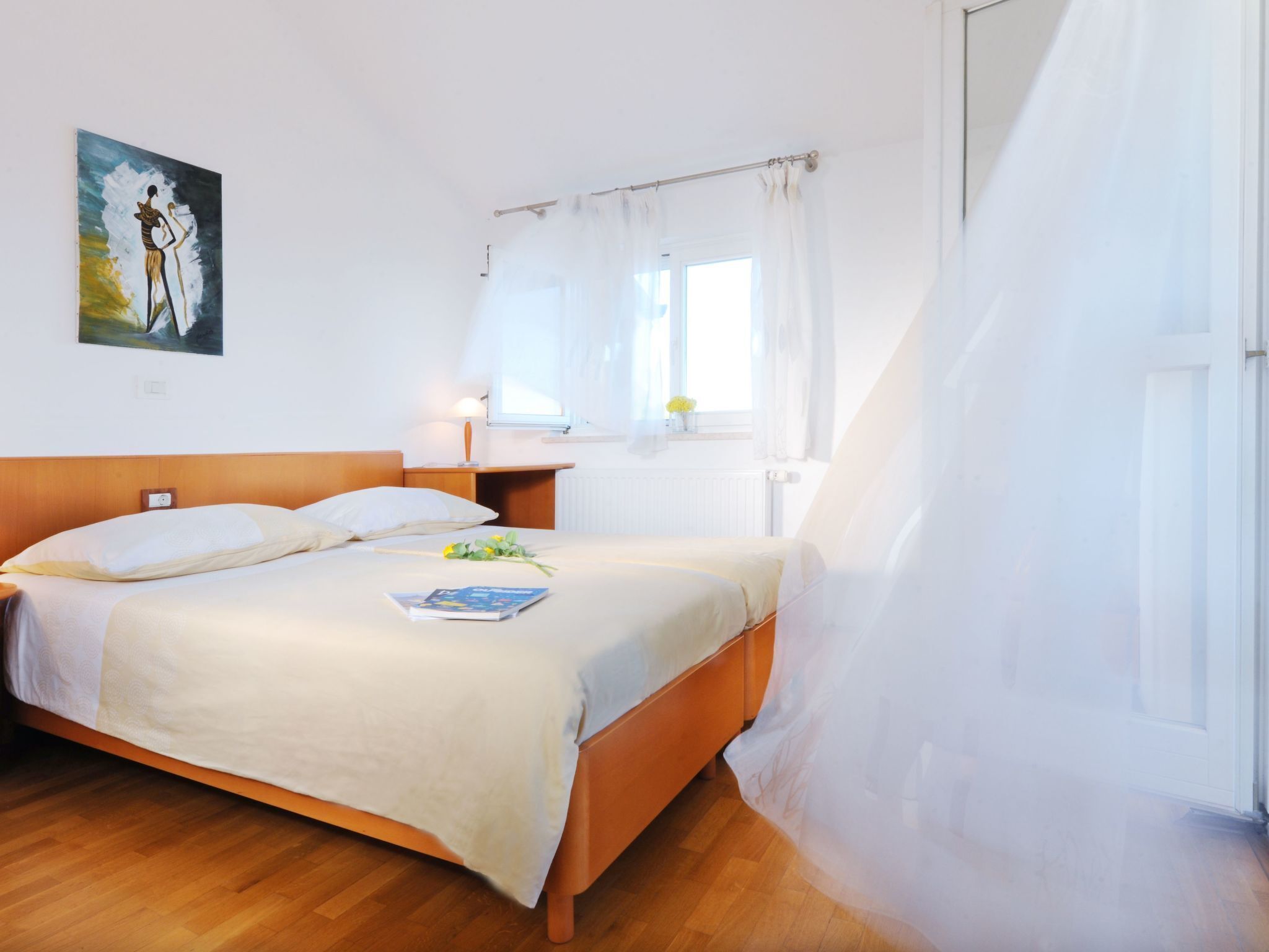 Une chambre d’hôtel avec un lit, une table de chevet avec une lampe, une fenêtre avec des rideaux et un tableau au mur.