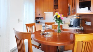 Zona pranzo con tavolo in legno, sedie, un vaso con fiori e pensili da cucina sullo sfondo.