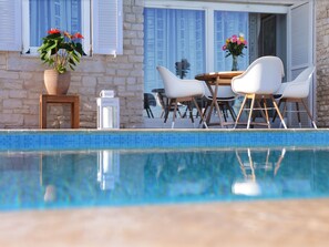 Un área junto a la piscina con mesa y sillas, una planta en maceta y un farol.
