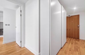 A corridor with white walls and wooden flooring, leading to a door. - Canary Wharf Skyline Retreat (London)