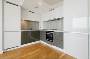 A modern kitchen with white cabinetry, a built-in oven, and a wooden floor. - Canary Wharf Skyline Retreat (London)