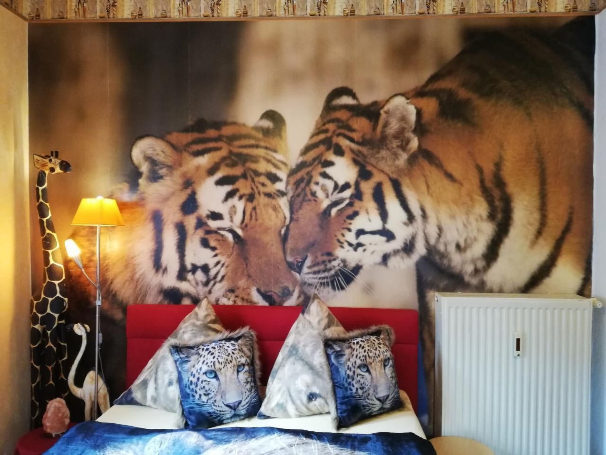 Ein Schlafzimmer mit einer großen Wandmalerei eines Tigers, einem roten Sofa, Leopardenkissen und einer Lampe.