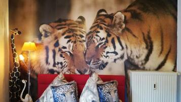 Ein Schlafzimmer mit einer großen Wandmalerei eines Tigers, einem roten Sofa, Leopardenkissen und einer Lampe.