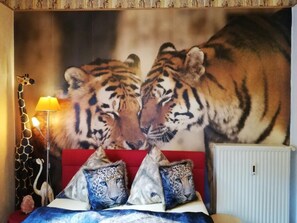 Ein Schlafzimmer mit einer großen Wandmalerei eines Tigers, einem roten Sofa, Leopardenkissen und einer Lampe.