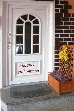 Eine weiße Tür mit Fenster und einem Willkommensschild.