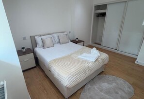 A bedroom with a bed, bedside tables, a wardrobe, and a round rug. - Executive 1 Bedroom Apartment- East Croydon (Croydon)